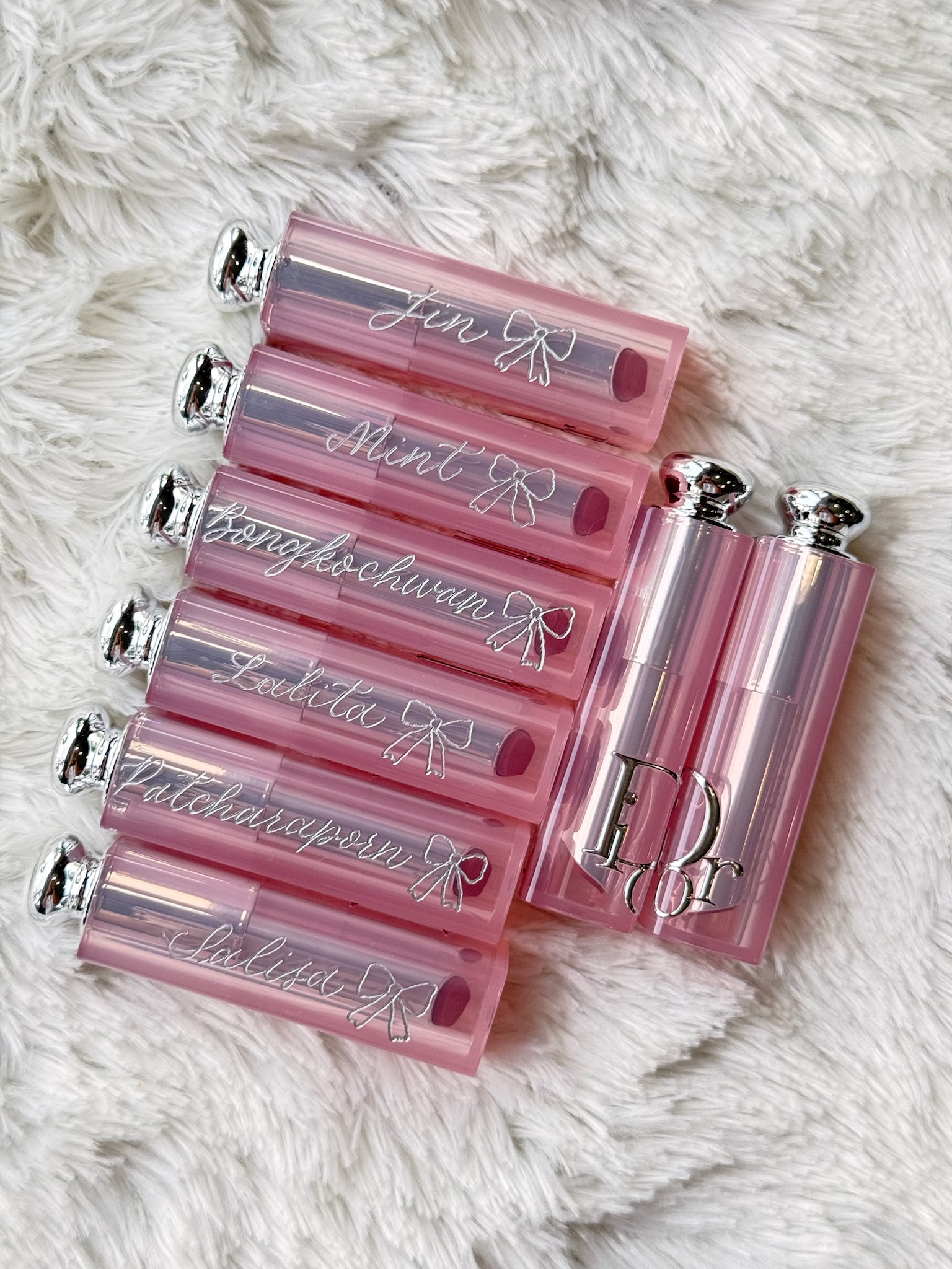 Six Dior Addict Lip Glow tubes stacked vertically, each with a calligraphed name and bow motif